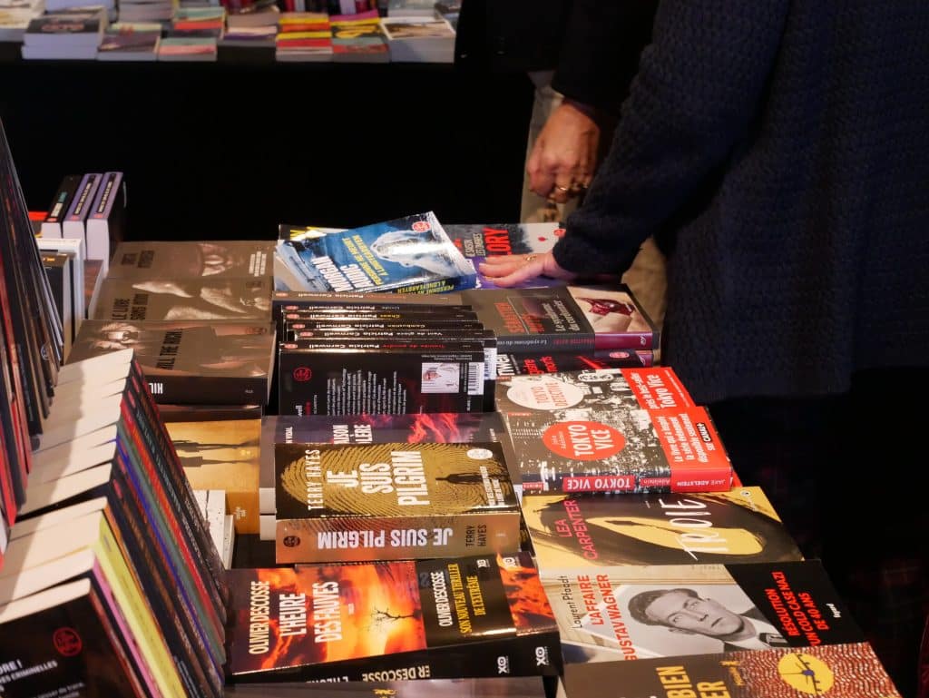 Photo avec une table de livres au salon des auteurs. Une main tapote un des livres sur la table.