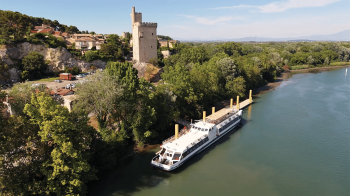 Bateau de fleuve point de vue du ciel, avec derrière une tour en pierre et un paysage avec des arbres