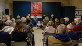 Table ronde dans une salle avec des intervenants à l'arrière plan et un public devant.